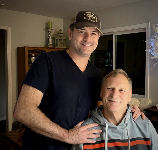 A portrait with his son Pete. Laren is sitting, while his son Pete is standing behind him. Both are smiling.