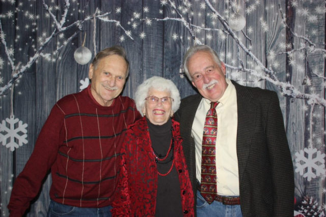 Church Christmas banquet photo - 2024 3 senior citizens posing in front of a Holiday decorated background.